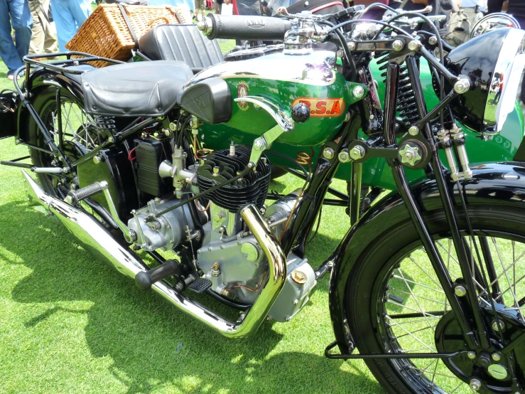 an old green motorcycle parked on grass next to people