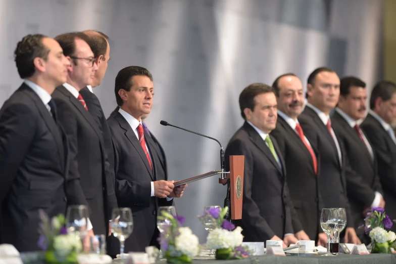 many men wearing suits and ties stand at a podium