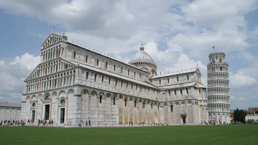 the leaning building has ornate towers near green grass