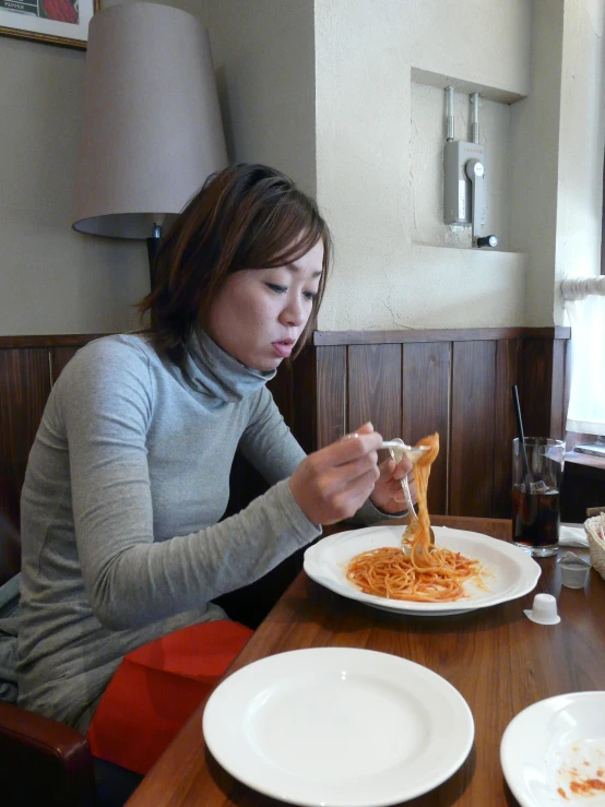 a woman in grey sweater eating spaghetti from a plate