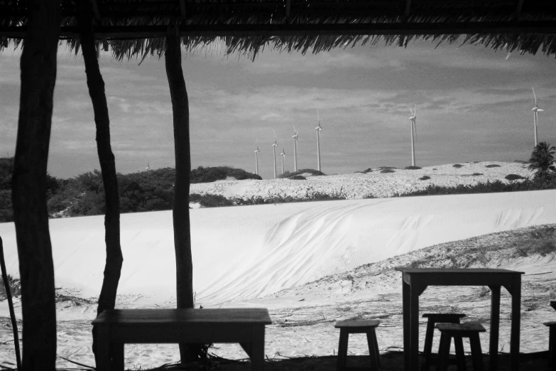 two wooden benches under an umbrella with wind mills in the background