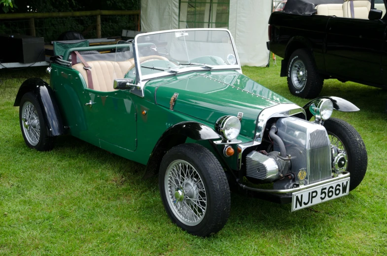 an old model green car parked on some grass