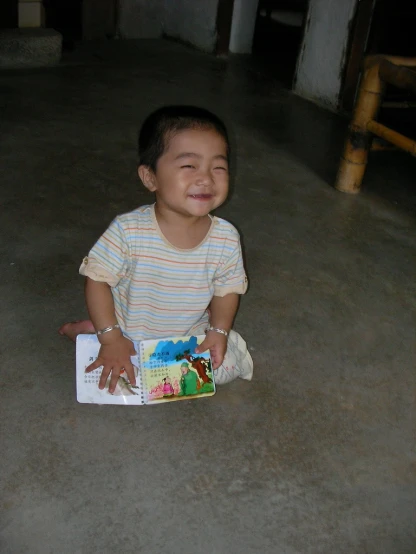 a little boy smiling while sitting down holding a book