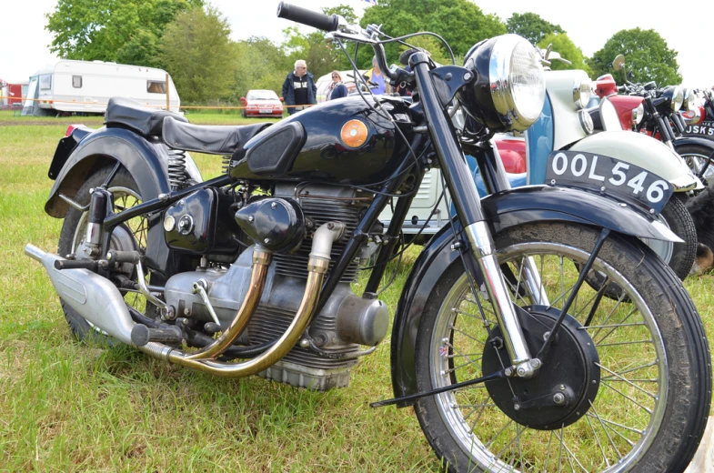 an old motorcycle parked on grass next to people