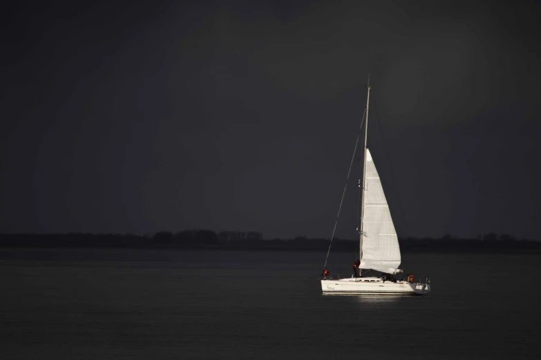 a boat with white sails floating in the dark water