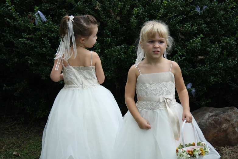 two girls standing side by side, one wearing a white dress