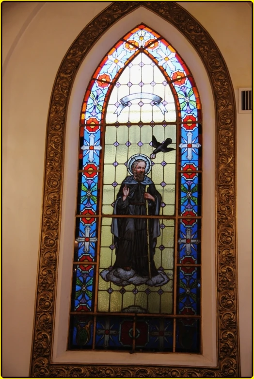 a stained glass window has the image of saint theresa holding a black bird