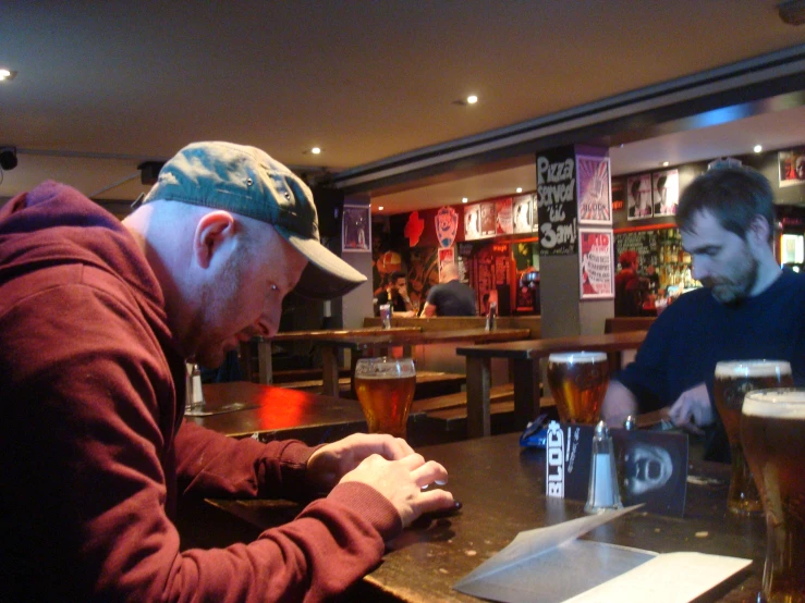 two men are sitting at a bar playing games with paper