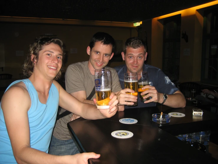 three young men posing for the camera holding glasses of beer
