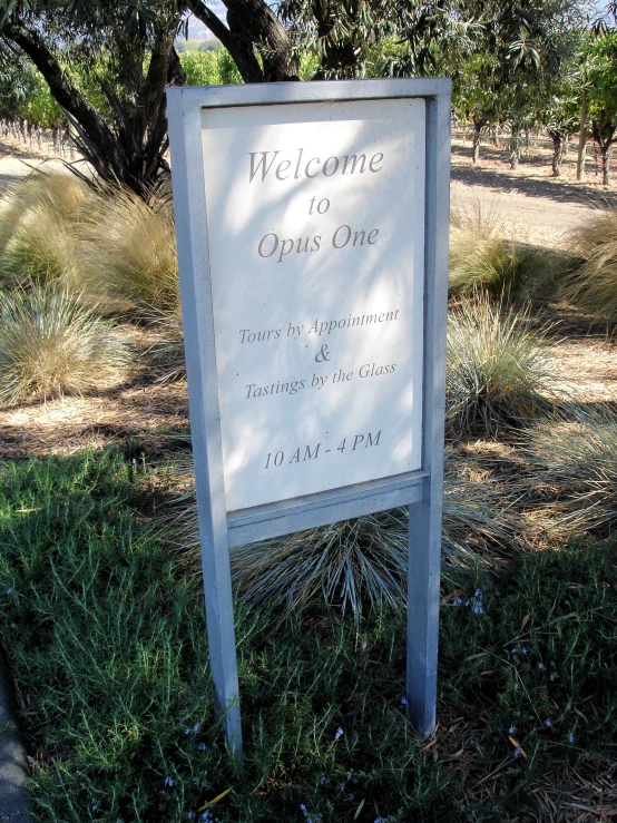 a welcome sign near some grass and trees