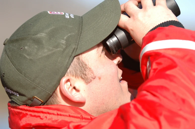 a man with a red coat holding a camera over his eye