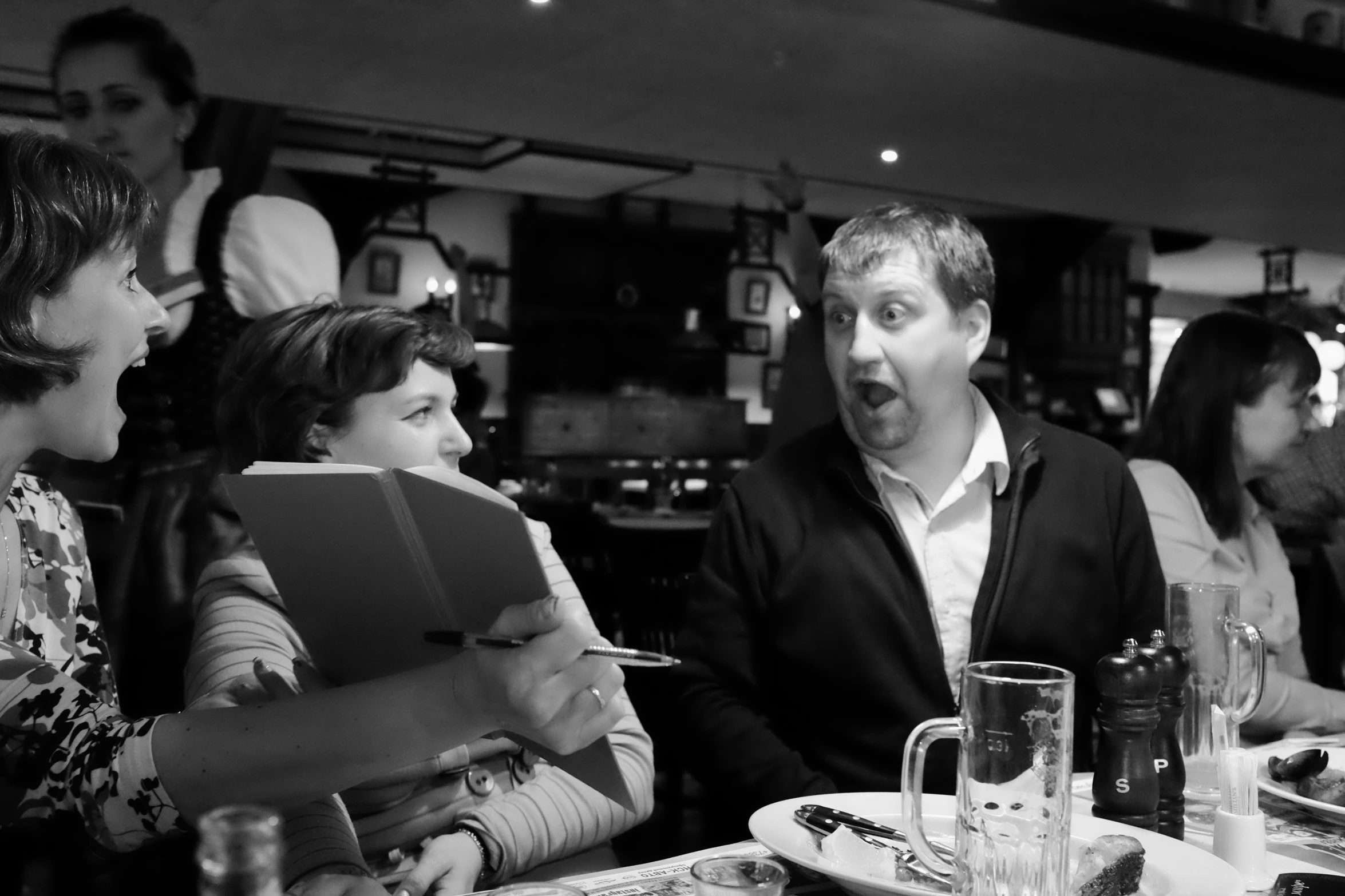 three people are sitting at a table while one person reads soing