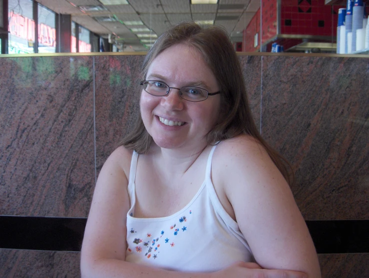 a woman in white tank top smiling and sitting at a table