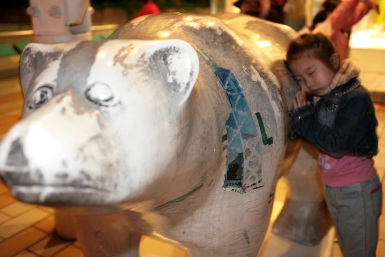 a little girl leaning on a large metal cow