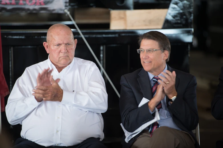 two men are sitting in a chair and clapping their hands