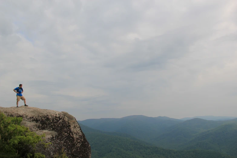 the man is standing on top of a large rock with mountains in the distance