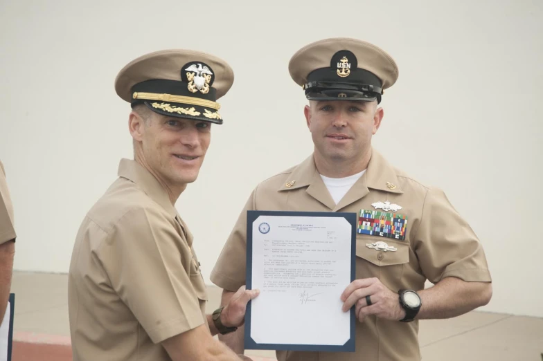 two navy officers in formal dress are holding a document
