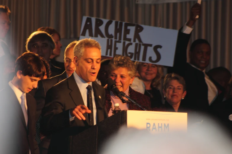 a man talking at a podium surrounded by people