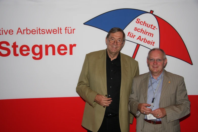 two men standing next to each other with a red and blue umbrella