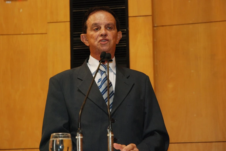 a man standing behind a microphone holding a wine glass