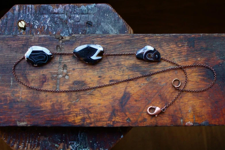 three pieces of jewelry hanging from chains on a wooden surface