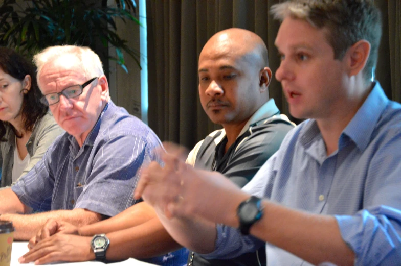 group of men sitting next to each other in front of a table