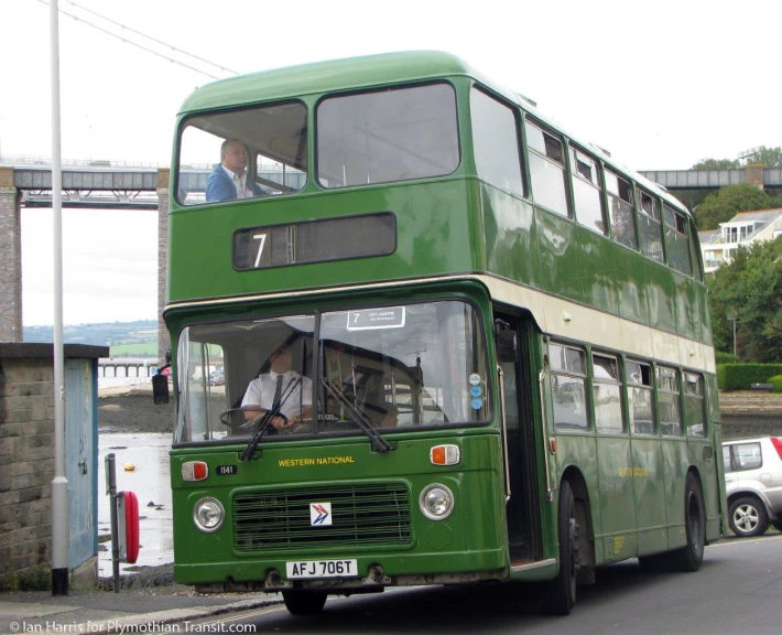 a green double decker bus is going down the road
