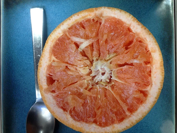 a gfruit sliced in half and a spoon on a blue plate