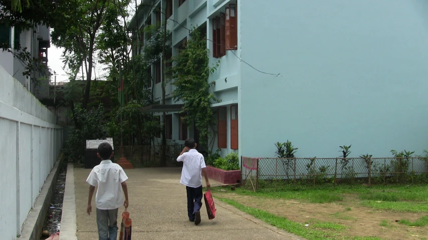 two men carrying luggage down a pathway next to some buildings