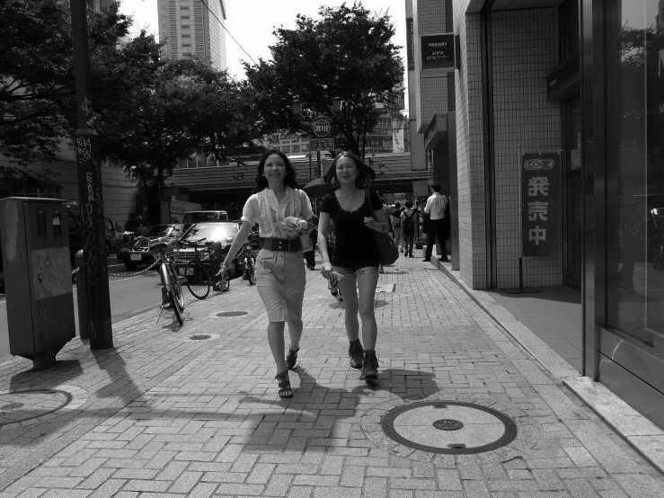 two girls are walking on a brick sidewalk in a city