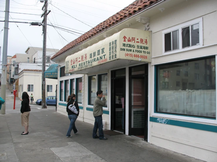 two people walking past a business with foreign writing on the outside