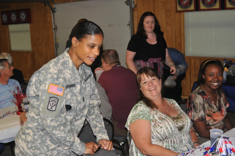 a female soldier is smiling while a group of people seated around her