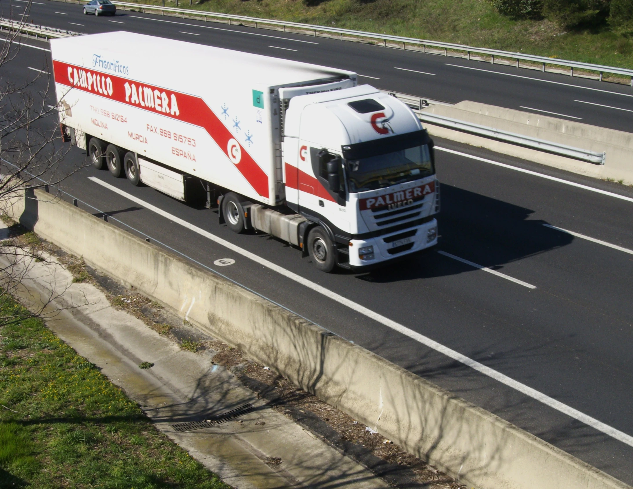 truck driving down highway next to trees in urban area