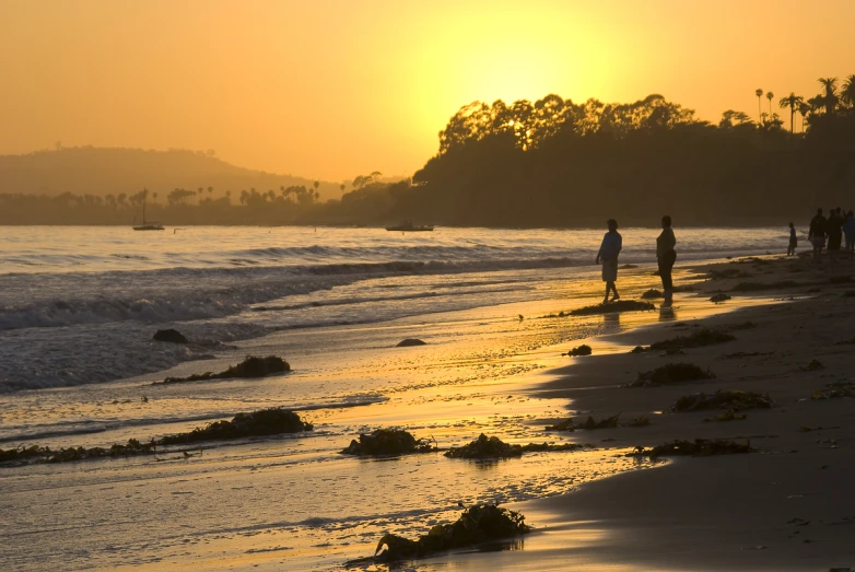 people are walking on the beach at sunset