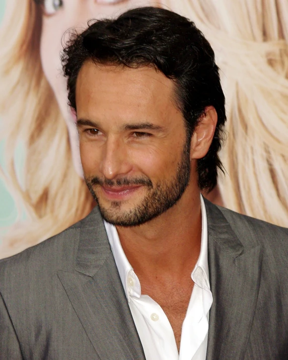 a man with long black hair and beard wearing a suit smiling at the camera