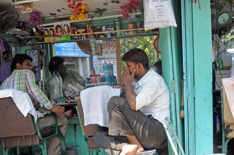 man sitting at an outdoor barber shop talking on his phone