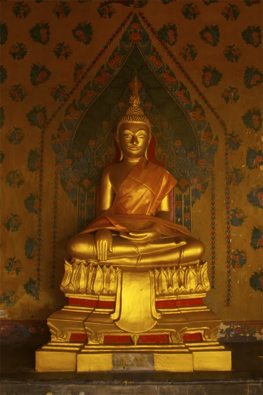 a gold buddha statue is sitting in front of a wall with colorful floral designs