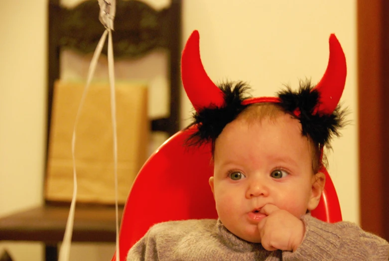 the baby wearing a devil costume is sitting on a chair