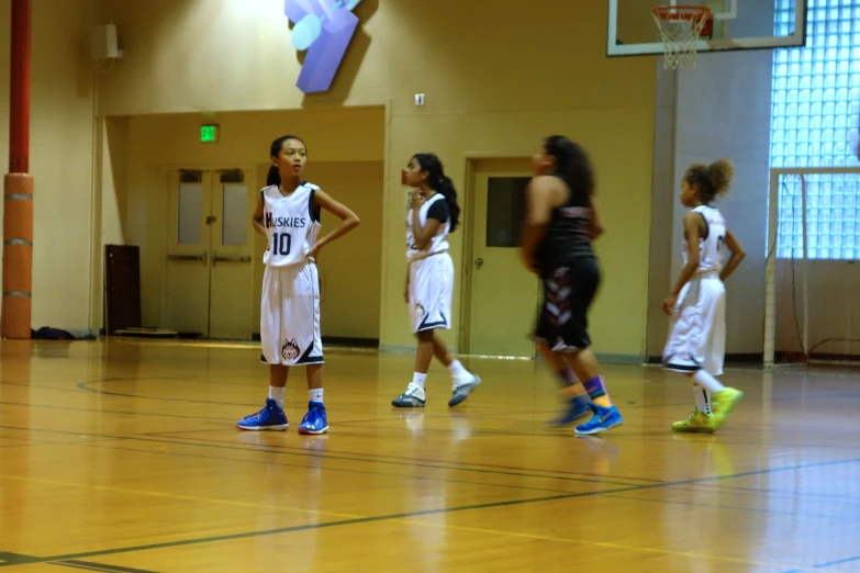 little girls in white and blue uniforms are playing basketball