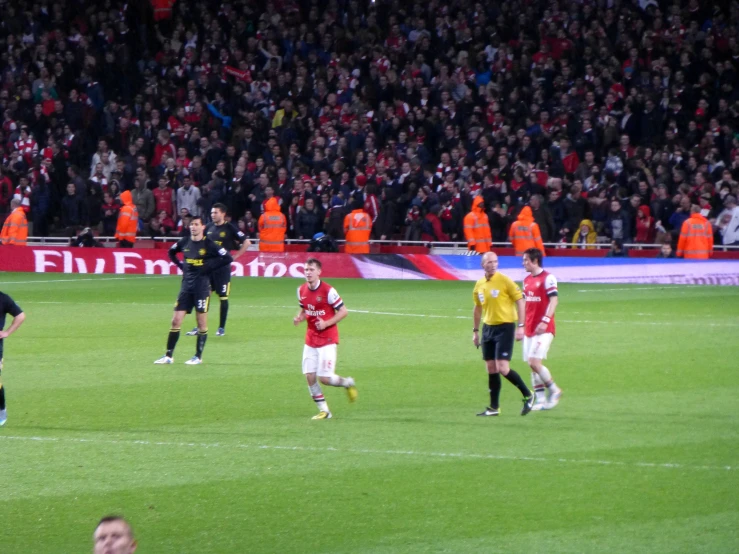 several players in red and black uniform walking around the soccer field