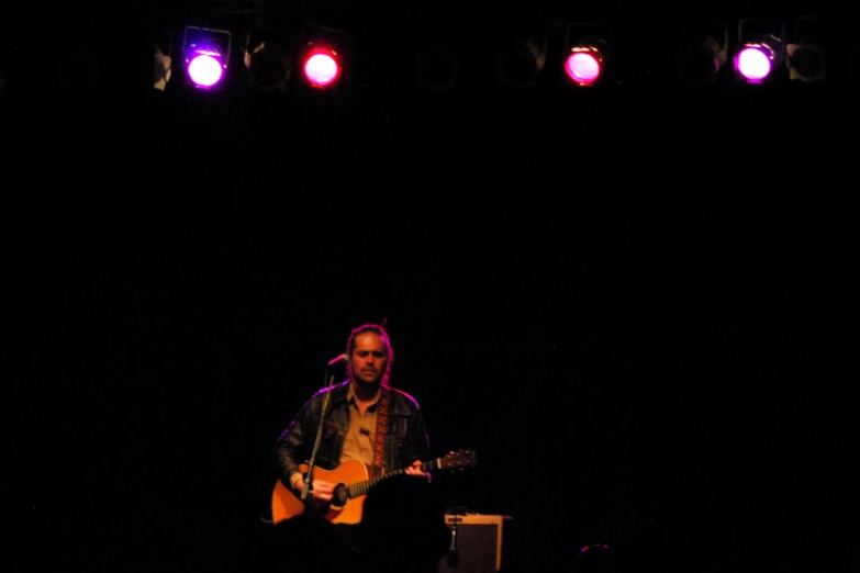 a man standing on stage playing guitar while lights shine down