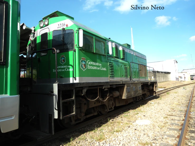 a green passenger train traveling down tracks in the day