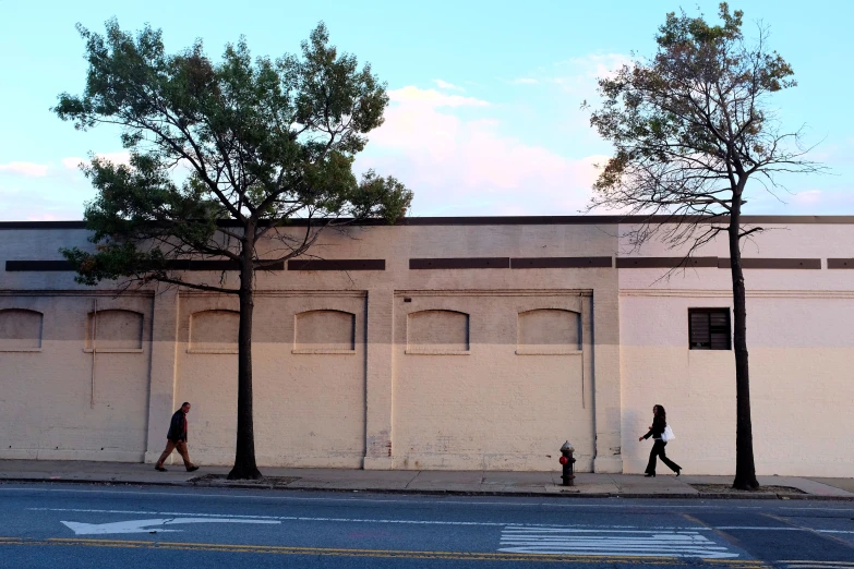 two people walking down the sidewalk past a large building