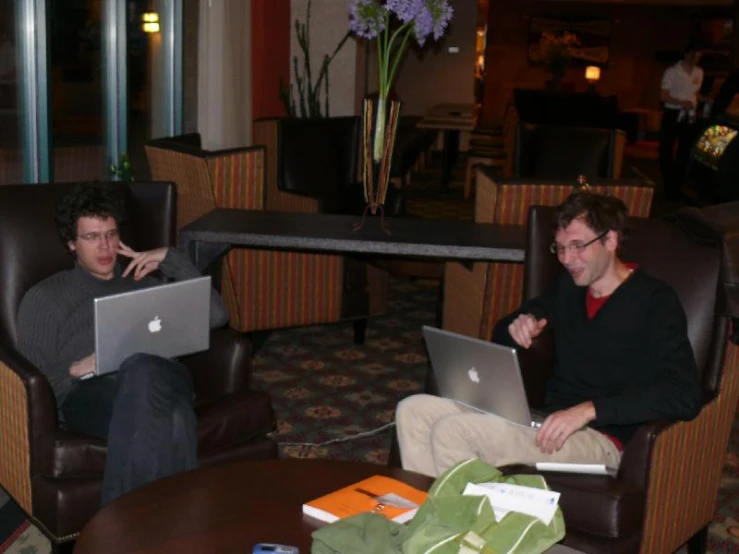 two men in chairs sit on laptops at a table