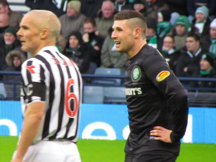 a man in a black and white uniform on a soccer field and another man in a black and white uniform is looking away from the camera