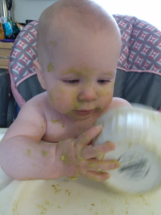 a baby playing in a high chair with some yellow food on his face