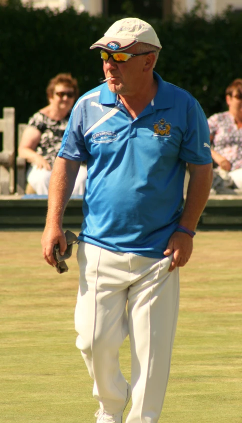 man wearing shades with a blue polo shirt and white pants, walks through the grass