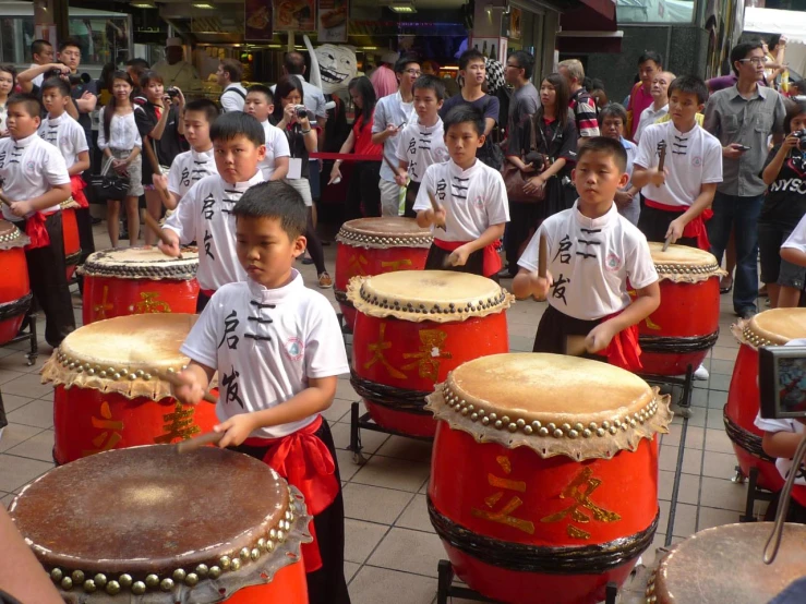 several children in white shirts are playing drums