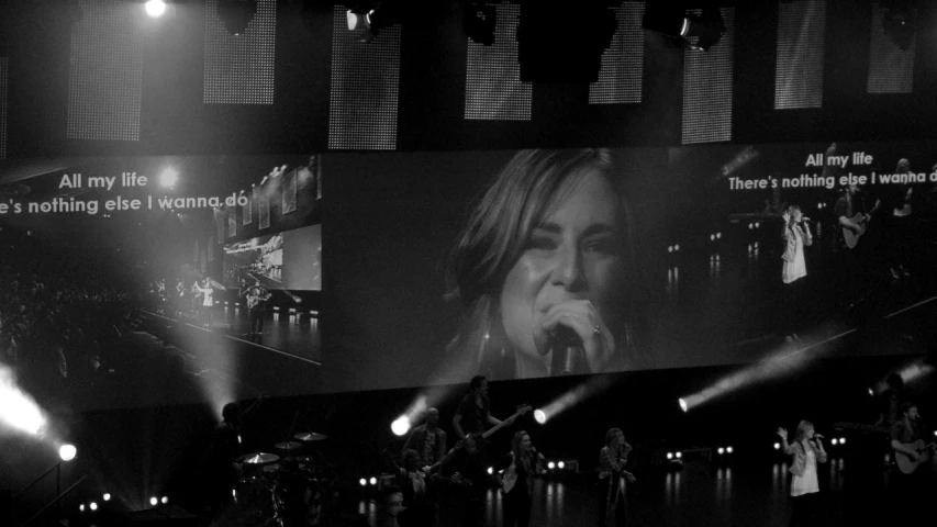 people singing on stage with a large screen behind them