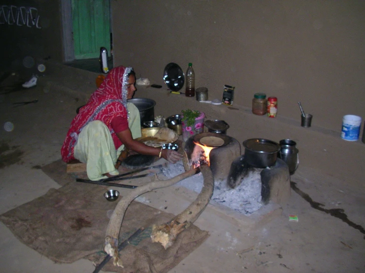 an old woman sitting next to a stove preparing food